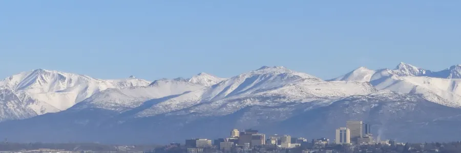 Long distance shot of the Anchorage skyline in winter, framed by snowy mountains